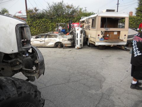 1986 Ford Bronco - Multiple wrecked vehicles and a bus are visible in a yard, with a large off-road vehicle in the foreground.