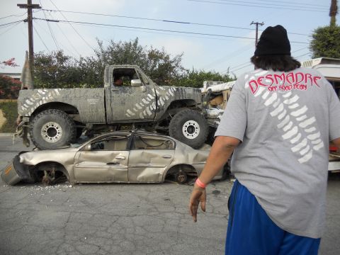 1986 Ford Bronco - A lifted pickup truck is parked on top of a severely damaged sedan.