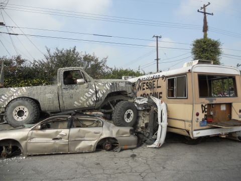 1986 Ford Bronco - A chaotic scene shows a lifted pickup truck crushing a sedan, with a bus nearby.
