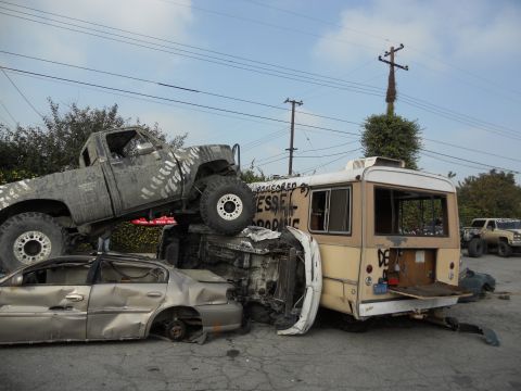 1986 Ford Bronco - A chaotic scene shows a heavily modified truck piled on top of a sedan and a bus, with visible graffiti on the bus.