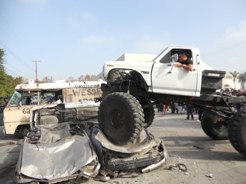 1986 Ford Bronco - A heavily modified white pickup truck is shown crushing a car, with a driver behind the wheel.