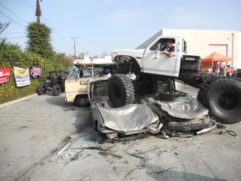 1986 Ford Bronco - A white pickup truck is positioned on top of several crushed cars, with other vehicles visible in the background.