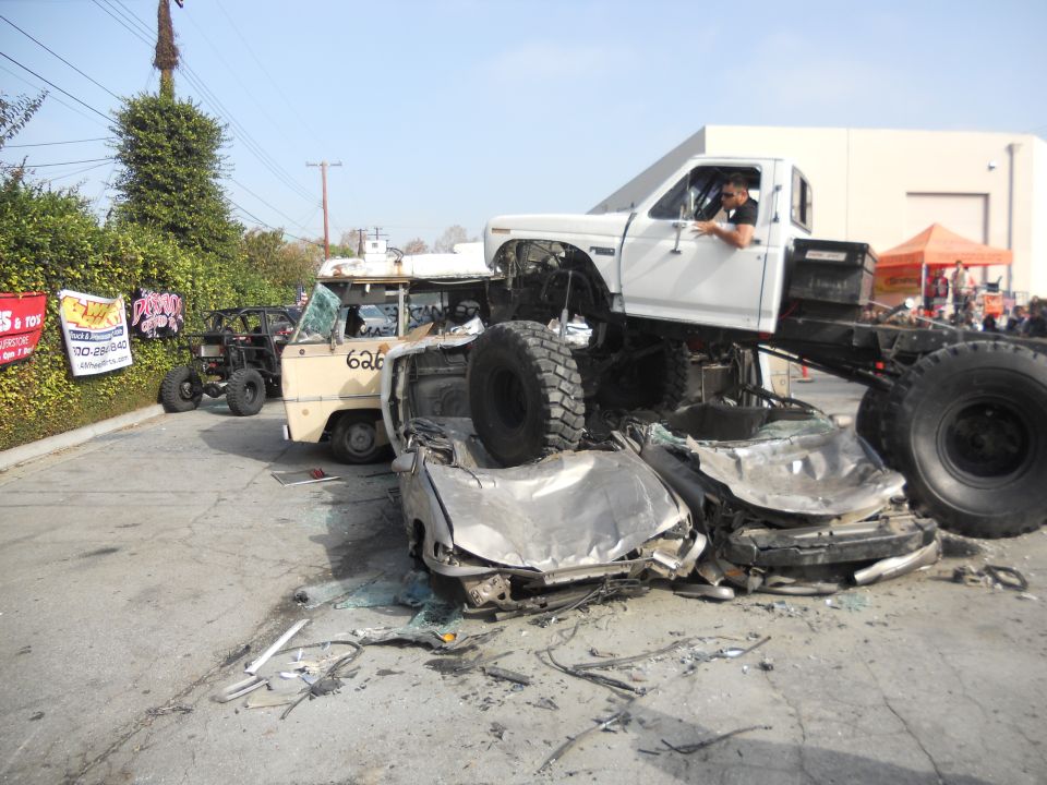 White pickup truck crushing cars, with a van and ATV in the background