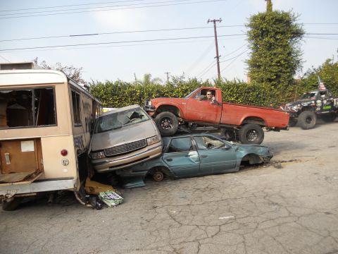 1986 Ford Bronco - Multiple wrecked vehicles are stacked and piled up in a yard.