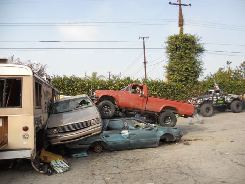 1986 Ford Bronco - Multiple vehicles are stacked and damaged in a junkyard setting.