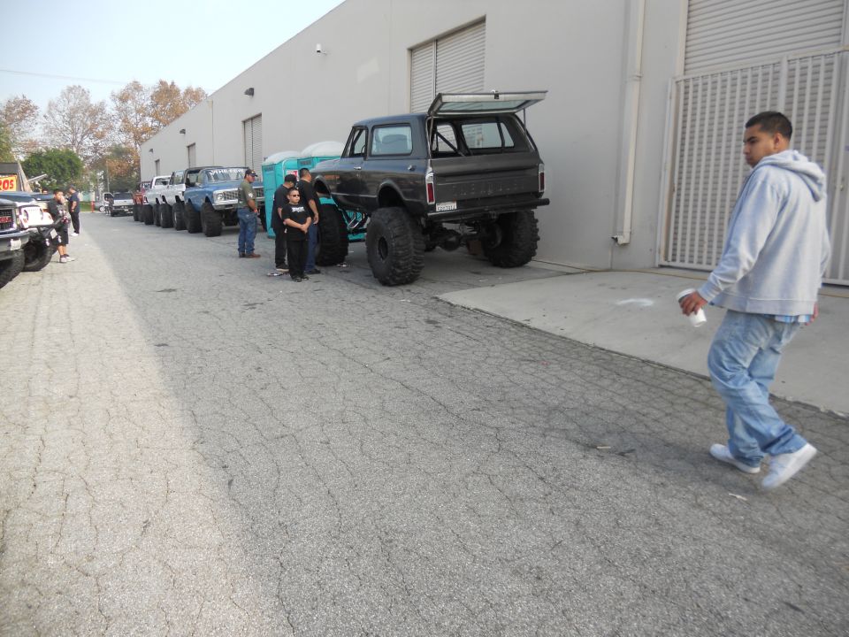 Several lifted SUVs and trucks are parked in a line outside a building. A man walks away from the camera