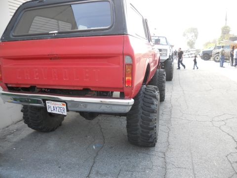 1986 Ford Bronco - A line of lifted off-road vehicles, including a red Chevrolet K5 Blazer, are parked on a street.