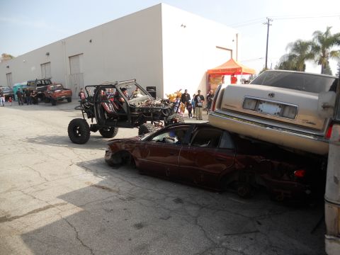 1986 Ford Bronco - A chaotic scene with a custom buggy crushing a sedan, while a Cadillac rests precariously on top of the buggy.