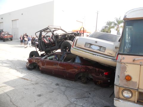1986 Ford Bronco - Multiple vehicles are piled up in a yard, including a custom off-road build and a bus.