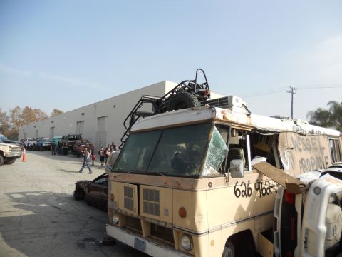 1986 Ford Bronco - A heavily modified RV, possibly a former school bus, is seen with a roll cage and spare tire mounted on its roof, alongside other vehicles.