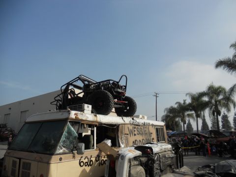 1986 Ford Bronco - A custom buggy is loaded onto the roof of a modified van, with a crowd gathered in the background.