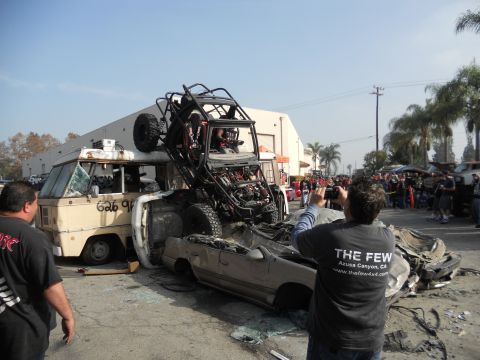 1986 Ford Bronco - A chaotic scene shows an off-road buggy precariously balanced on a van, with a wrecked car below.