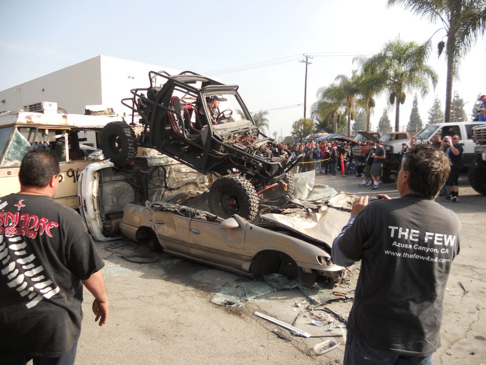 Off-road buggy atop a crushed car, with spectators watching