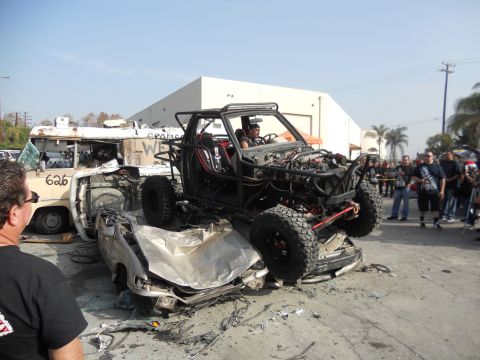 1986 Ford Bronco - A heavily modified off-road buggy is perched atop a severely damaged car, with a wrecked van nearby.