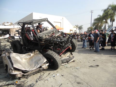 1986 Ford Bronco - A heavily modified off-road buggy is shown perched atop a severely damaged car, with spectators in the background.