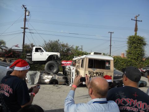 1986 Ford Bronco - A lifted pickup truck is parked on top of several wrecked cars, with a van in the background.