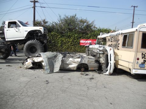 1986 Ford Bronco - A scene of destruction shows a crushed car caught between a monster truck and a graffiti-covered bus.