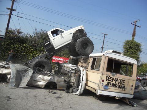 1986 Ford Bronco - A monster truck has crushed several vehicles, including a bus, in a chaotic scene.