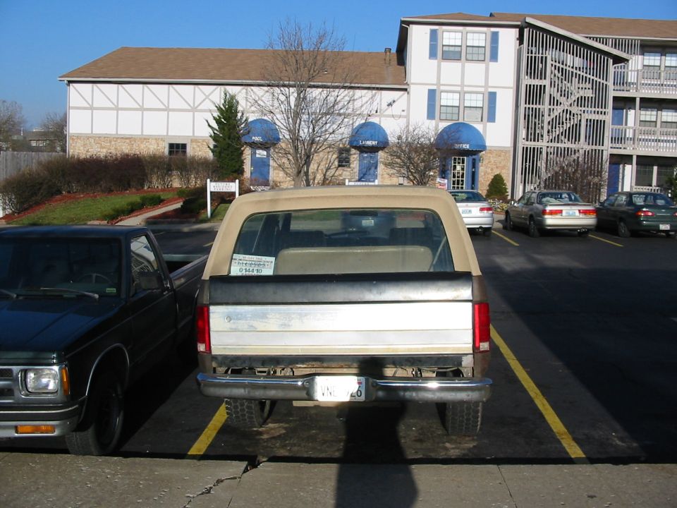 Rear of tan crew-cab pickup parked at an apartment complex, S-10 to its left