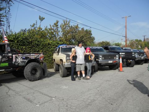 1986 Ford Bronco - Several modified off-road vehicles are parked in a lot, with a group of people standing in front of them.