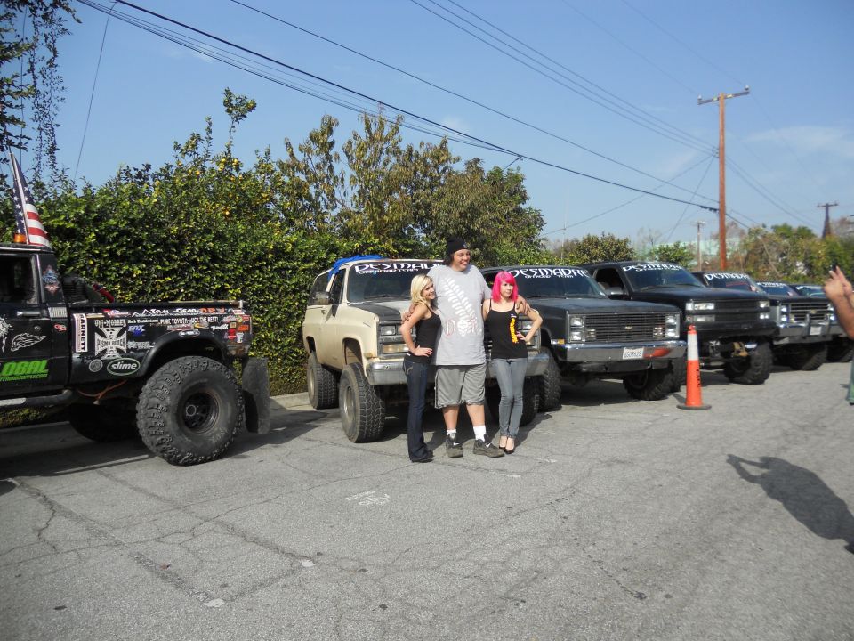Group posing with lifted trucks and SUVs, one with an American flag