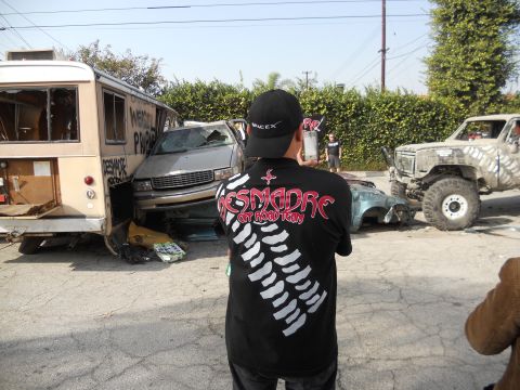 1986 Ford Bronco - A collection of damaged vehicles and a person observing the scene, with a large off-road truck in the background.
