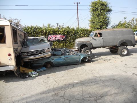 1986 Ford Bronco - Multiple vehicles are in disarray, with a lifted panel truck parked nearby.