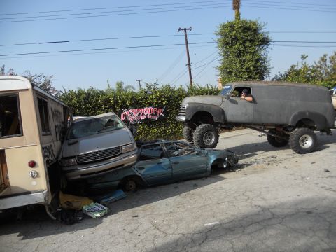 1986 Ford Bronco - A custom panel van is parked near several wrecked cars and a bus.