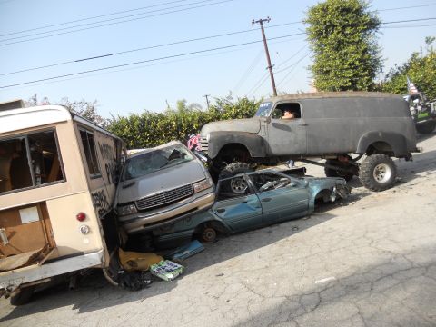 1986 Ford Bronco - A collection of damaged vehicles and a heavily modified panel van are piled up on a street.