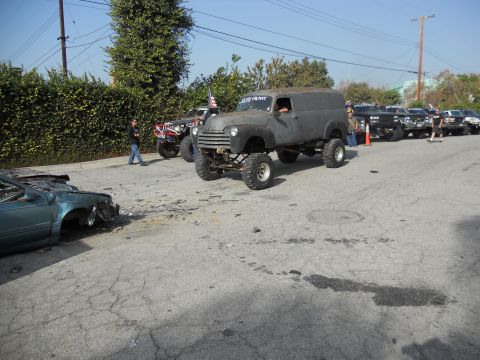 1986 Ford Bronco - A heavily modified panel van with off-road tires is parked on a street, with other vehicles in the background.