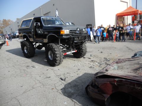 1986 Ford Bronco - A heavily modified Bronco is parked next to a wrecked car, with onlookers in the background.