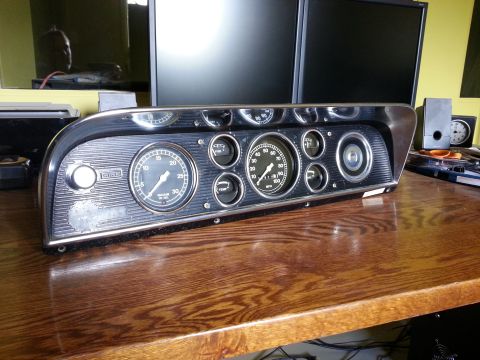 1967 Ford F-100 - A vehicle's instrument cluster with various gauges is displayed on a wooden desk.