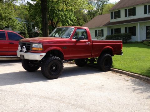 1996 Ford F-150 - This lifted 1996 Ford F-150 pickup truck is shown in a residential driveway with a house and trees in the background.