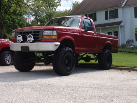 1996 Ford F-150 - This lifted 1996 Ford F-150 pickup truck is parked on a paved surface in front of a residential building.