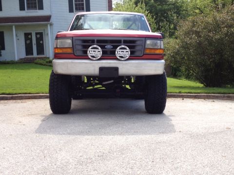 1996 Ford F-150 - This red pickup truck is shown from the front, a lifted suspension and aftermarket lights.