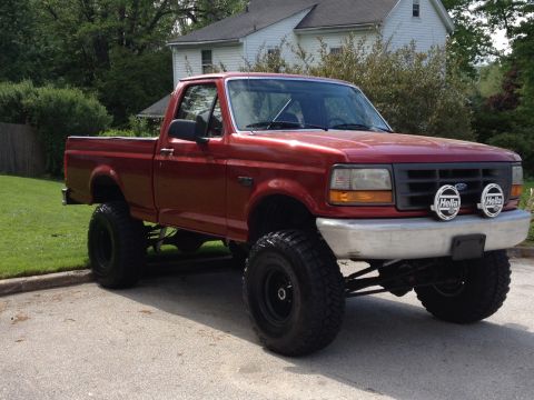 1996 Ford F-150 - A lifted red pickup truck with aftermarket lights on the front bumper is parked on a paved surface.