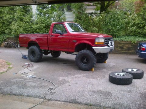 1996 Ford F-150 - A red 1996 Ford F-150 pickup truck is shown with its front end raised by a jack, and spare tires are on the ground.