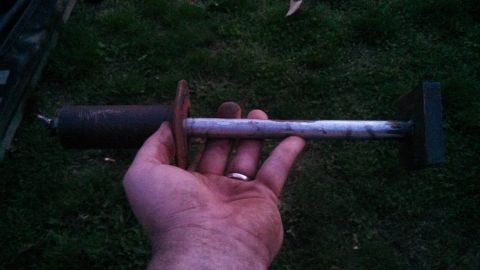 1979 Ford Bronco - A hand holds a metal part, possibly a tool or component, with distinct cylindrical and rectangular ends.