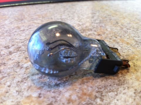 1996 Ford F-150 - A used light bulb with visible internal filaments and blackened glass sits on a speckled surface.