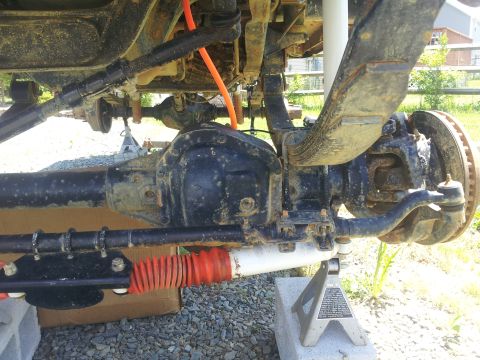 1988 Ford Bronco - Undercarriage view shows the rear axle, leaf springs, and steering linkage of a vehicle supported by jack stands.