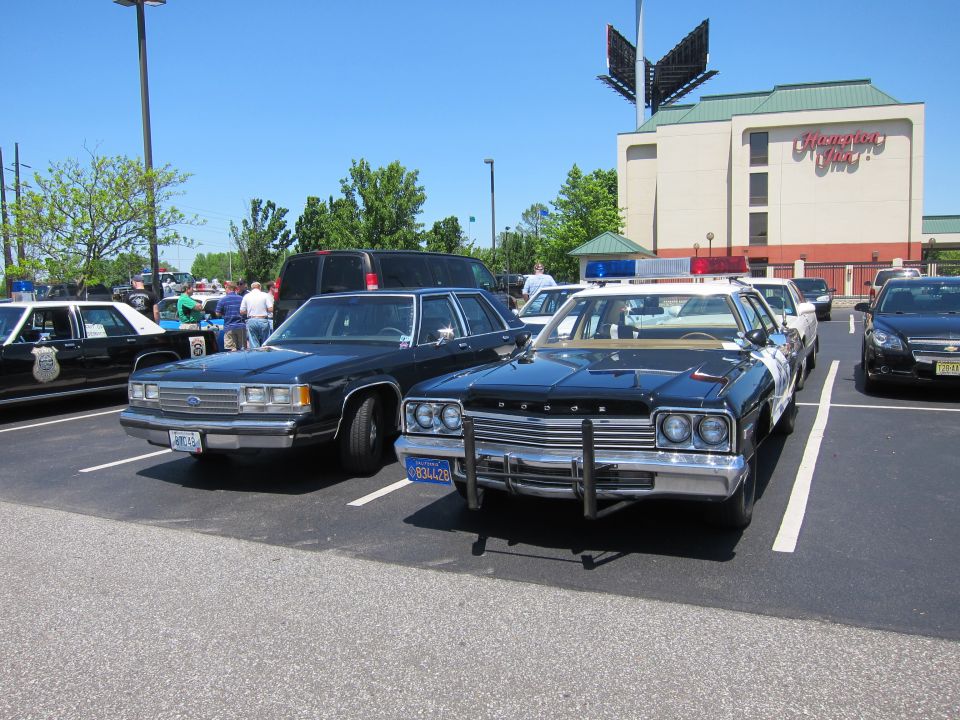 Black Dodge police sedan with push bar beside a Ford cruiser at a parking-lot car show