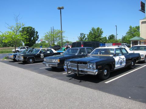 1991 Ford LTD Crown Victoria - row of vintage cruisers including a black-and-white Highway Patrol Dodge sedan with push bar parked in a sunny lot.