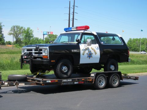 1991 Ford LTD Crown Victoria - black-and-white Highway Patrol Dodge Ramcharger SUV with light bar sits strapped on a flatbed trailer outdoors.