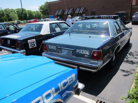 1991 Ford LTD Crown Victoria - Rear view of a blue State Police Ford sedan with Out of Service light bar, flanked by a black-and-white cruiser and a blue Police car.