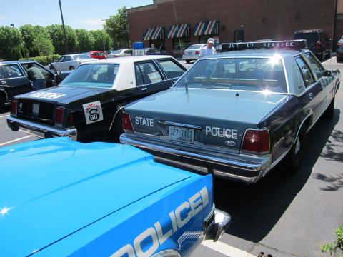 1991 Ford LTD Crown Victoria - Rear three-quarter view of a blue State Police Ford sedan with light bar parked among black-and-white and blue cruisers.