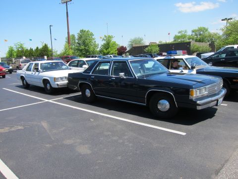 1991 Ford LTD Crown Victoria - dark blue Ford LTD Crown Victoria sedan parked beside a white station wagon among cruisers in a sunny lot.