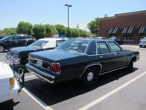 1991 Ford LTD Crown Victoria - Rear three-quarter view of a dark blue Ford LTD Crown Victoria sedan parked among cruisers near a brick building.
