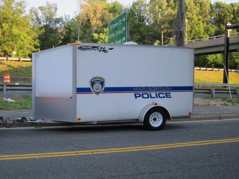 1991 Ford LTD Crown Victoria - white enclosed cargo trailer with a Marlborough Police badge and blue stripe parked at the side of a road near a guardrail.