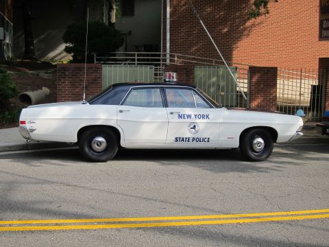 1991 Ford LTD Crown Victoria - white New York State Police sedan with a blue roof, door seal, and roof light parked at the curb in front of a brick building.