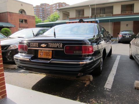 1991 Ford LTD Crown Victoria - black Chevrolet Caprice marked STATE TROOPER with a roof lightbar sits parked outside a hotel beside other cars.